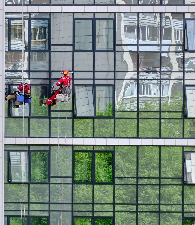 Two industrial climbers from the cleaning service wash the glass facade of a modern high-rise apartment building. Rope access